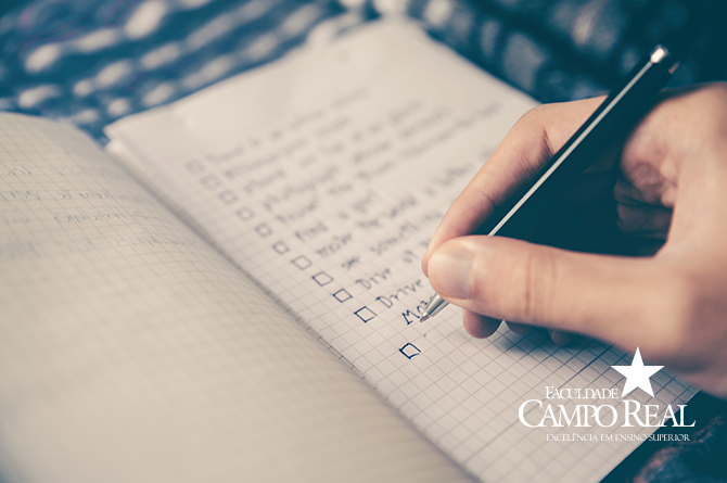 Foto de uma mão com uma caneta escrevendo em um caderno quadriculado - post enem
